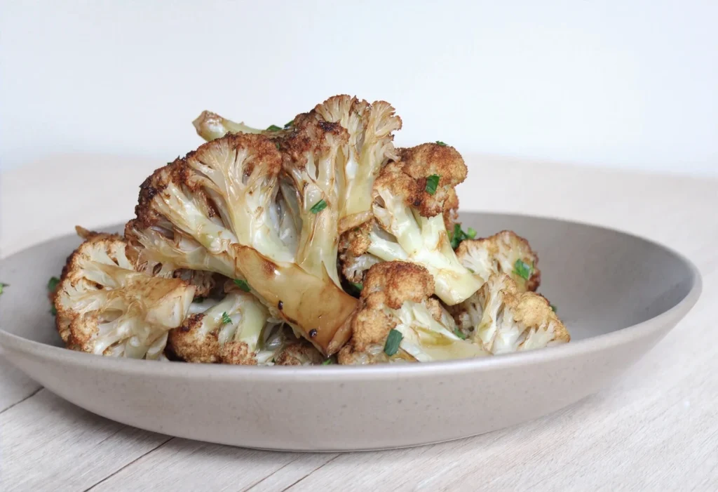 Pysznie przypieczony kalafior w bułce tartej, posypany świeżą pietruszką, na szarym talerzu. Zdjęcie idealne na bloga kulinarnego.